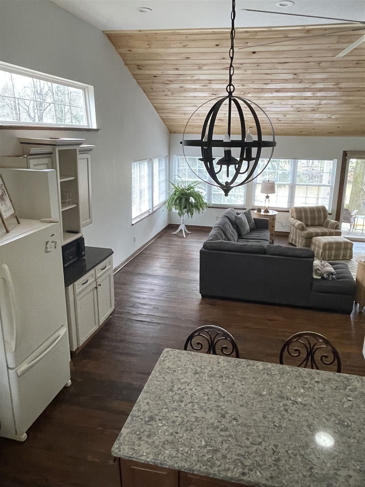 Vaulted great room with knotty-pine ceiling, granite island, and wall of windows facing the river