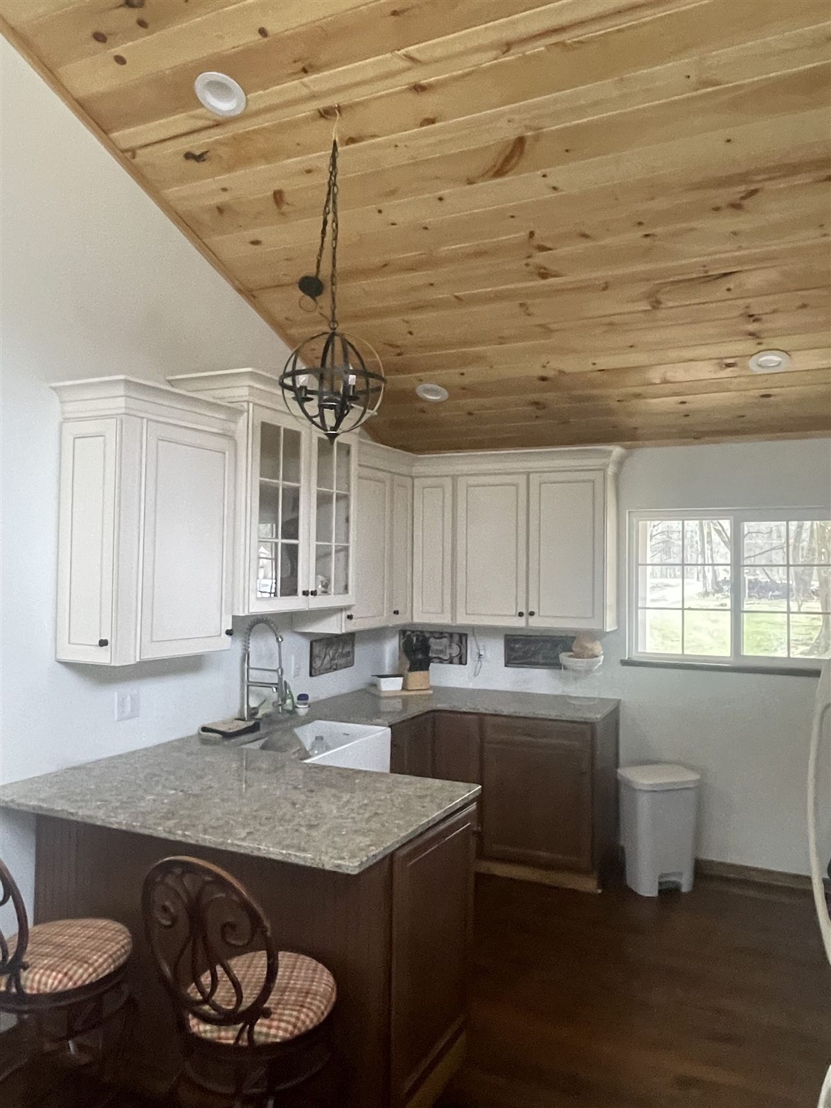 Kitchen with white cabinetry, granite counters, farmhouse sink, and knotty-pine ceiling